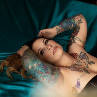 Beautiful woman with blue tattoos wears a black corset while posing for a plus size boudoir photographer in Tampa, FL